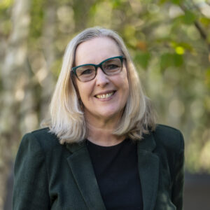 Blonde woman wearing glasses and a green coat with a black shirt